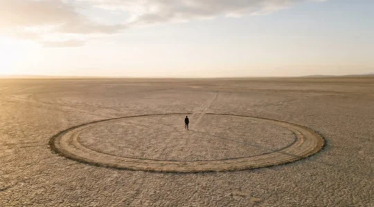 Une personne se tenant au centre d'un chemin circulaire tracé dans le sable, symbolisant deux années passées à tourner en rond sans trouver la sortie.